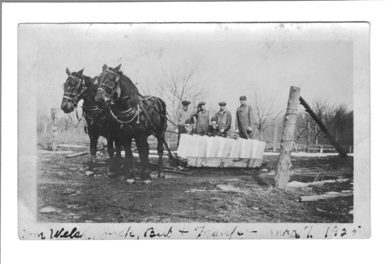 Two-horse team pulling a sledge of ice blocks on Francis Noble's farm, men standing behind, 1925