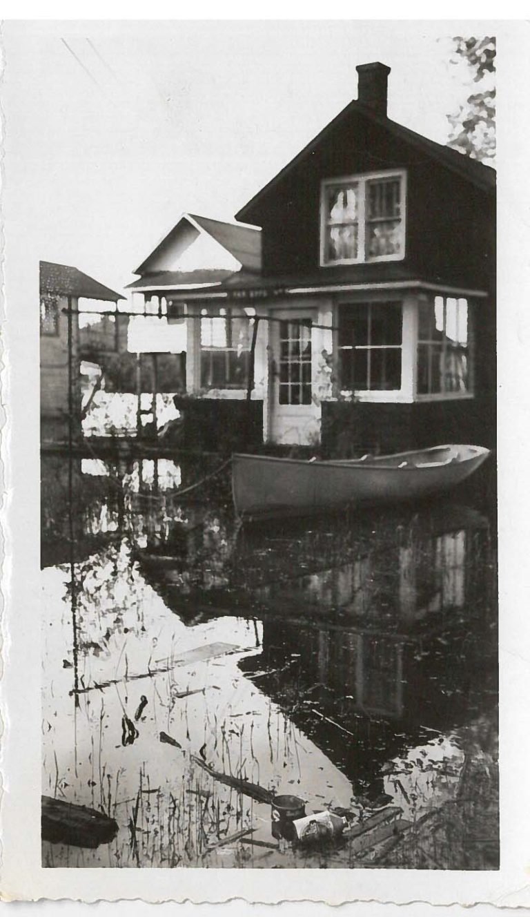 Floodwater surrounding a two-story cottage, a rowboat floating by its front windows