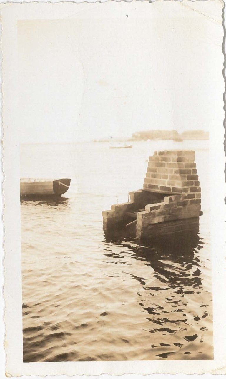 Sepia snapshot of a brick structure standing in the water, a rowboat nearby and a distant shore