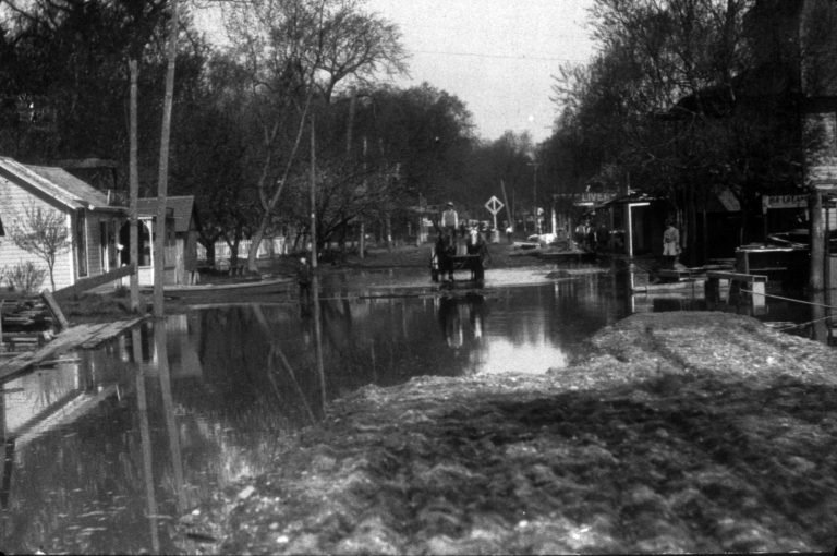 Flooded village street with a horse and wagon wading through and buildings along both sides