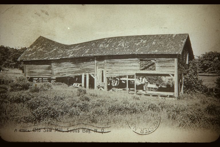 Postcard 'Old Saw Mill, Sodus Bay, N.Y.': weathered open-sided wooden mill building in tall grass