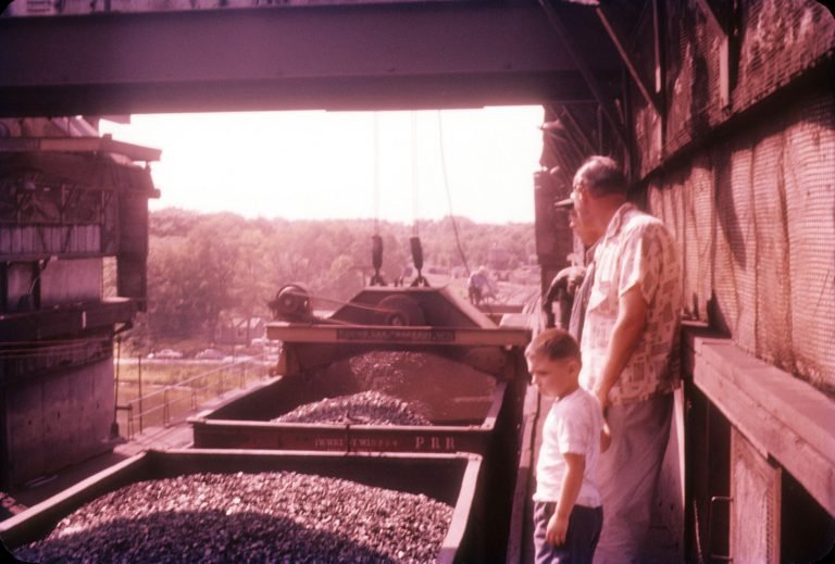 Man and boy on top of the coal trestle, looking down at railcars heaped with coal beneath a hoisting machine