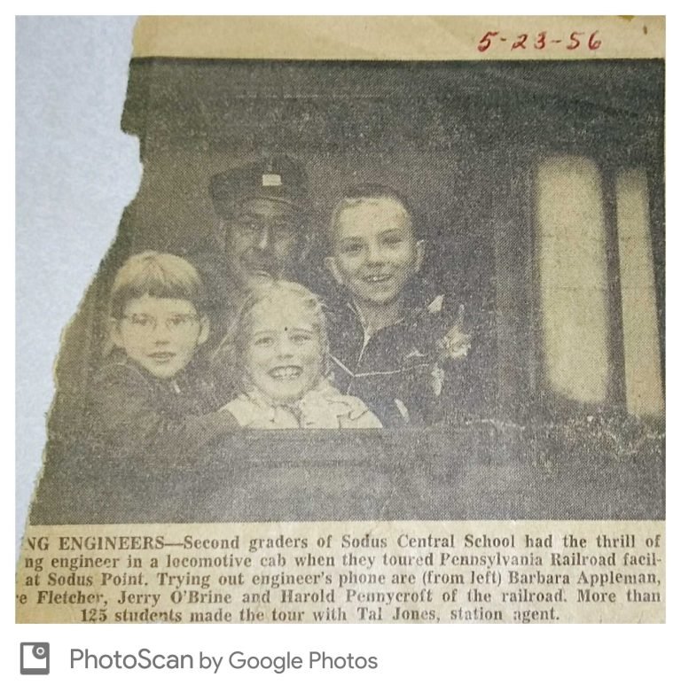 Newspaper clipping dated 5-23-56 of three smiling children and a railroad man in a cap at a locomotive cab window