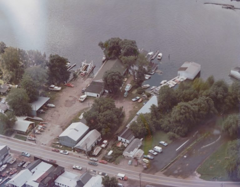 Aerial view of waterfront buildings, docks and parking along a road, the roller skating rink at center