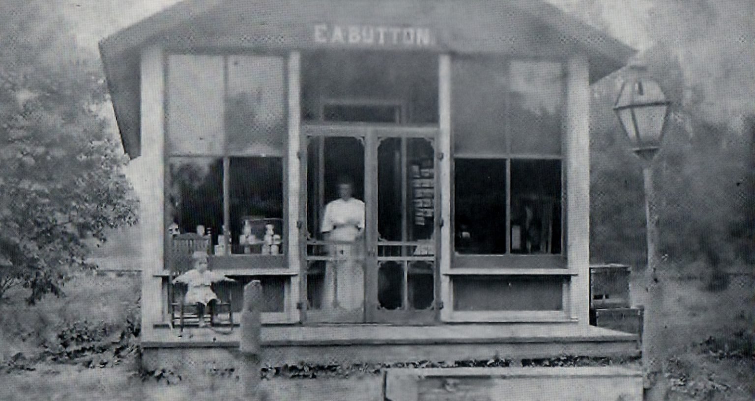 E. A. Button store, a glass-fronted shop with a woman in the doorway and a child seated on the porch