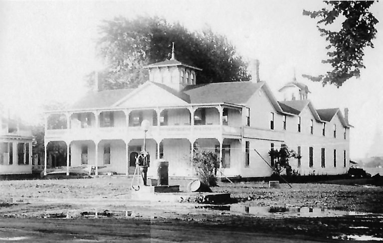 Bay Shore House, a large two-story building with double verandas and a rooftop cupola, facing a muddy yard