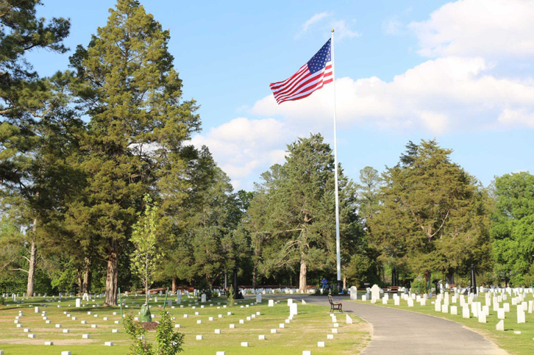 Poplar Grove National Cemetery: rows of small white headstones on a lawn beneath a tall U.S. flag and pines