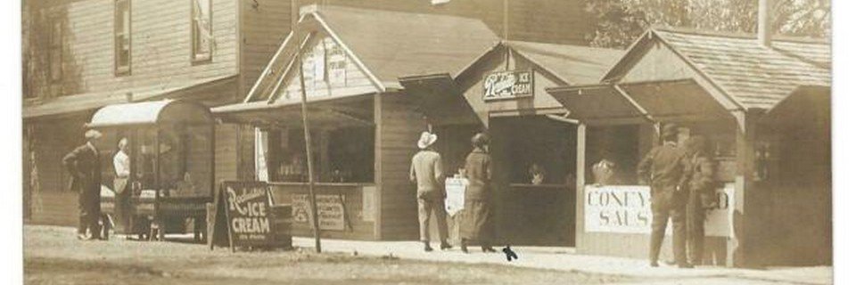 Sepia view of small wooden food stands with ice cream and Coney signs, people standing out front