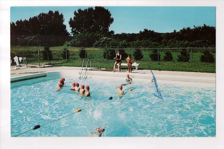 Postcard of the Camp Beechwood pool, swimmers in red caps along lane ropes and two people on a bench
