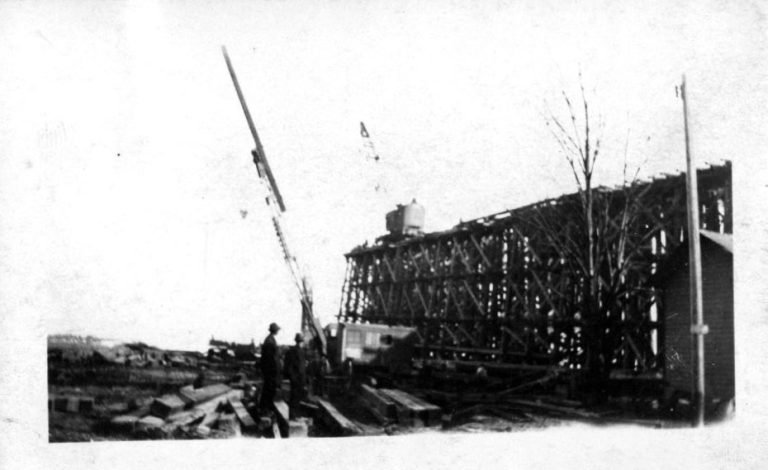 Timber framework of the coal trestle under construction, a crane boom raised and workmen among stacked beams