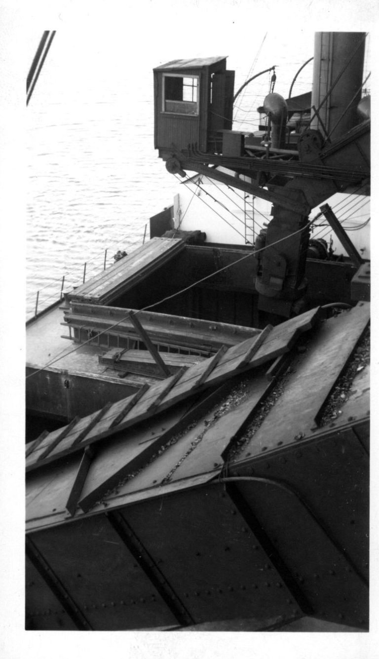 View down from the coal trestle onto a ship's open hatch, a steel loading chute and an operator's cab