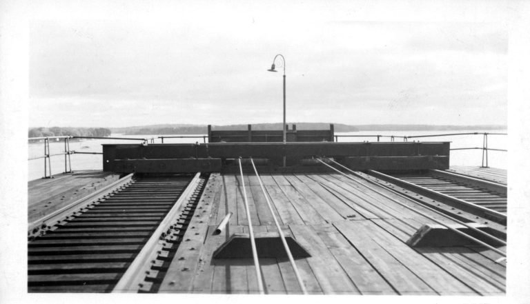 Top deck of the coal trestle, rails ending at a timber bumper and lamppost, with the bay beyond