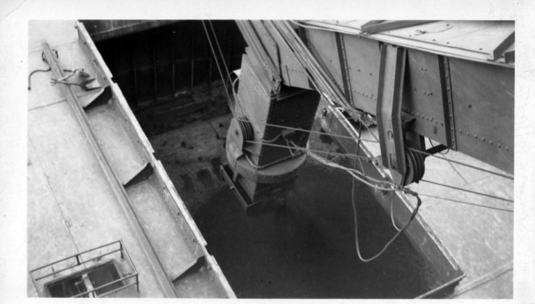 Looking down from the coal trestle as a loading chute on cables is lowered into a ship's open cargo hold