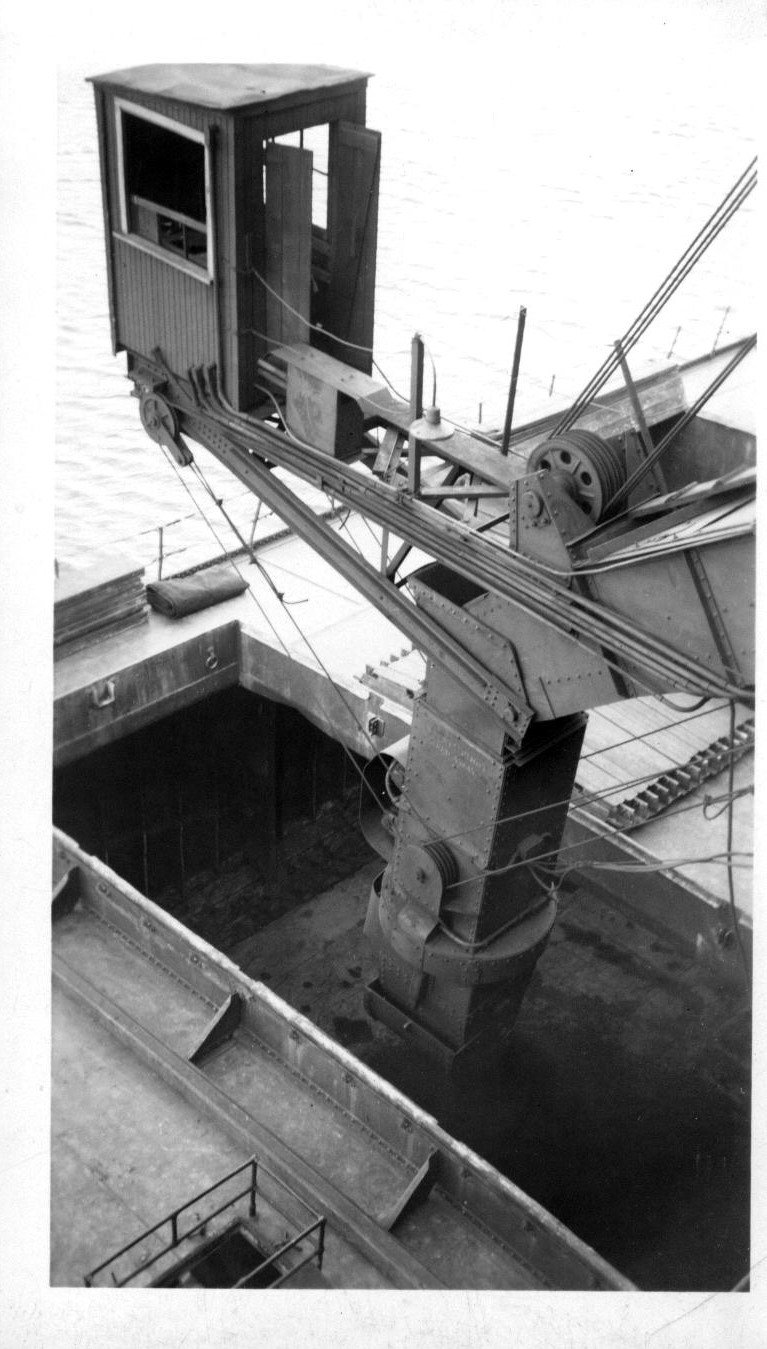 Loading chute machinery with an operator's cab, lowered into the open cargo hold of a ship below