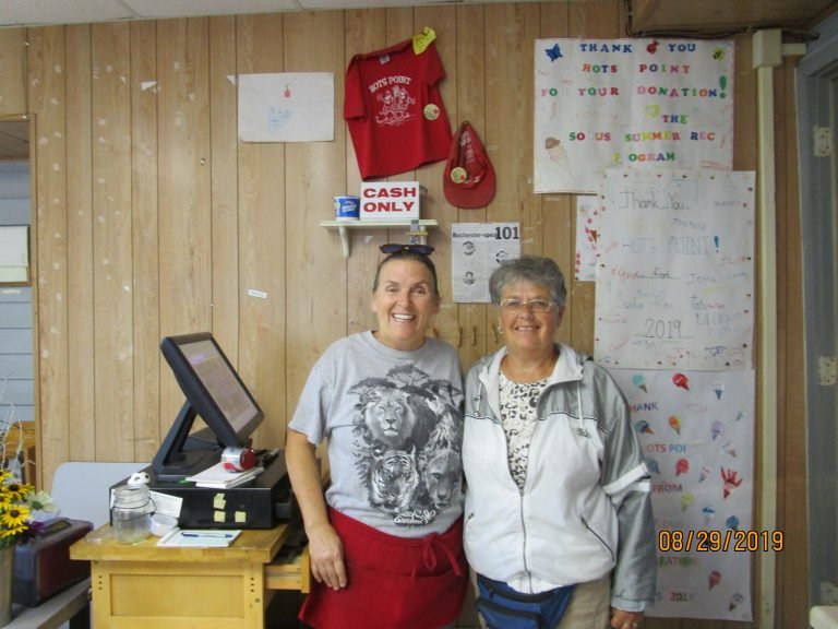 Two smiling women at a snack-stand counter beside thank-you posters for Hots Point from the Sodus Summer Rec program