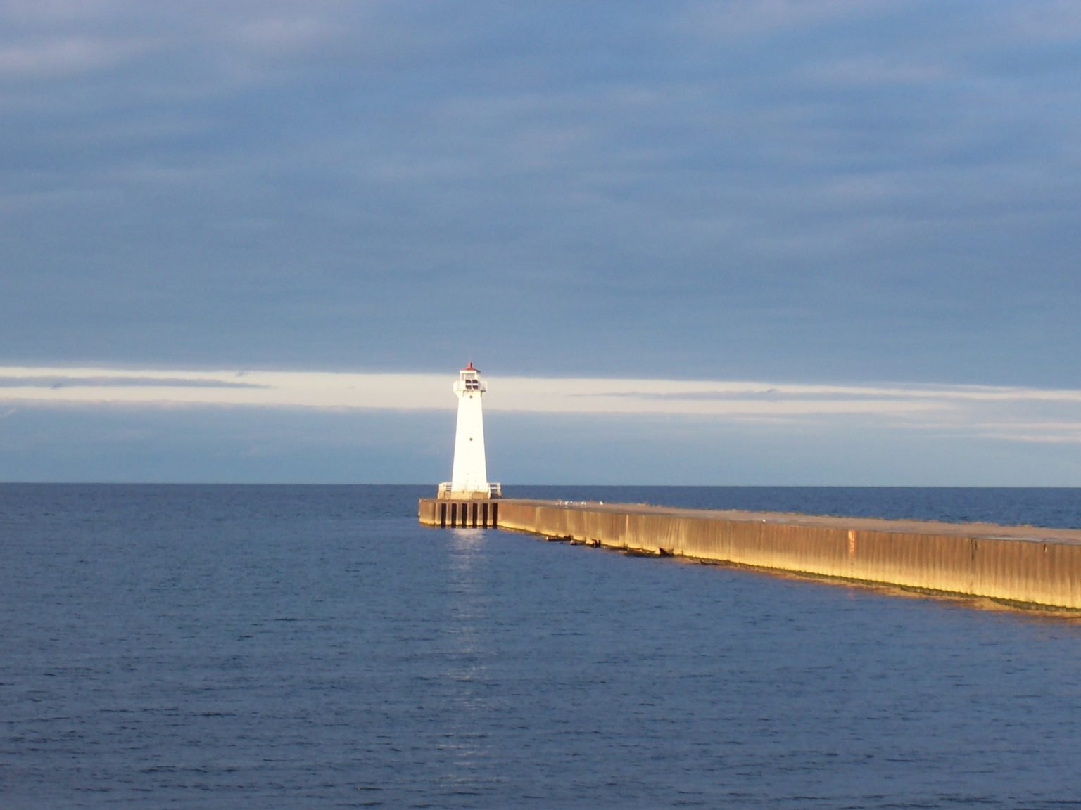 The remaining outer pier light, a white tower at the end of a long concrete pier, lit by low sun