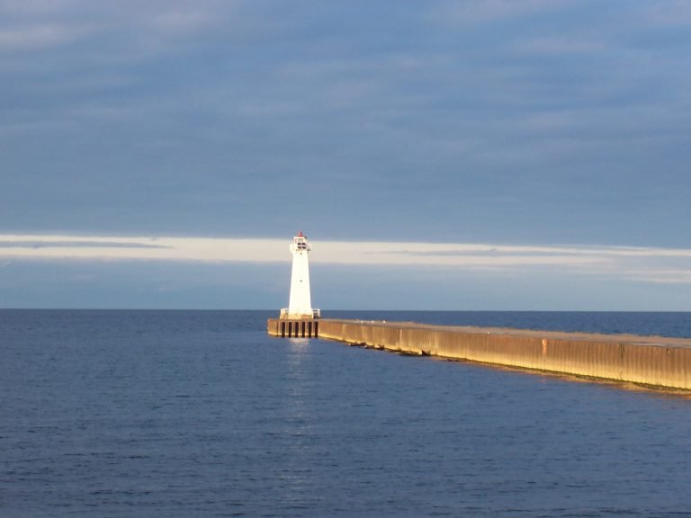 The remaining outer pier light, a white tower at the end of a long concrete pier, lit by low sun