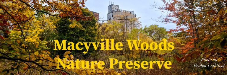 Banner reading 'Macyville Woods Nature Preserve' over autumn trees, a tall concrete industrial building rising behind