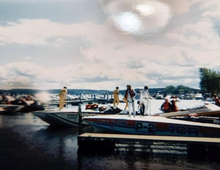 Racing powerboats tied up at a dock, crew in jumpsuits standing on the decks, one boat marked 'P-2'