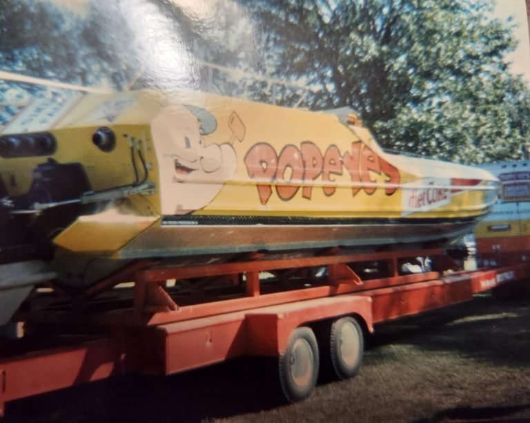 Yellow racing powerboat lettered 'Popeyes' with a cartoon character and a Diet Coke logo, on an orange trailer
