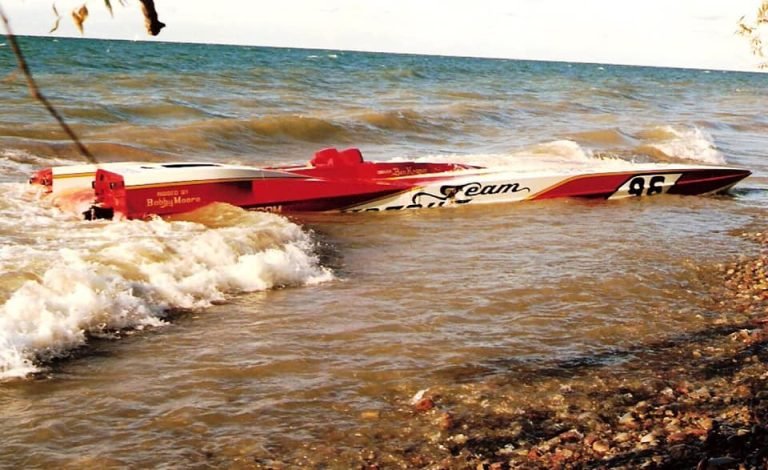 Team Apache's red and white racing powerboat, number 96, washed up on a stony shore in the surf
