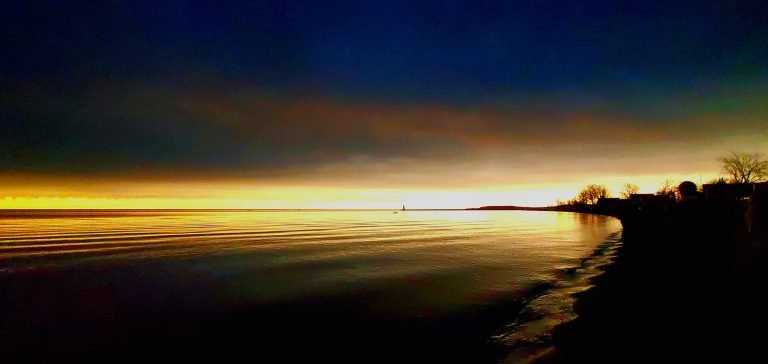 Lake under a darkened sky during the eclipse, a golden glow along the horizon, the shoreline in silhouette