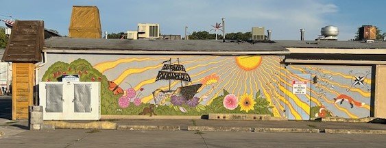 Mural of a sailing ship under a large radiating sun, with flowers and butterflies, on a long low building